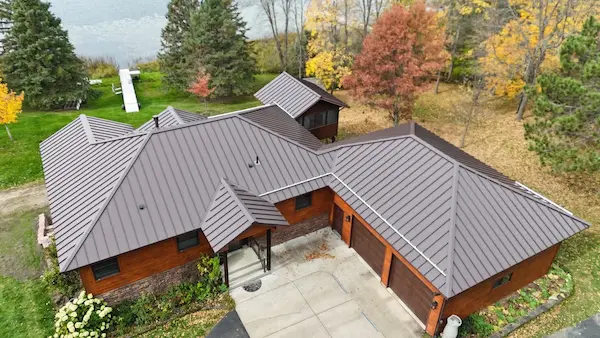 Custom-bent metal roof installation on a large residential property surrounded by autumn trees in Aitkin, MN
