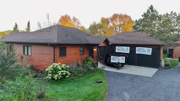 Finished dark standing seam metal roofing on a wood-sided home with a detached garage in Aitkin, Minnesota